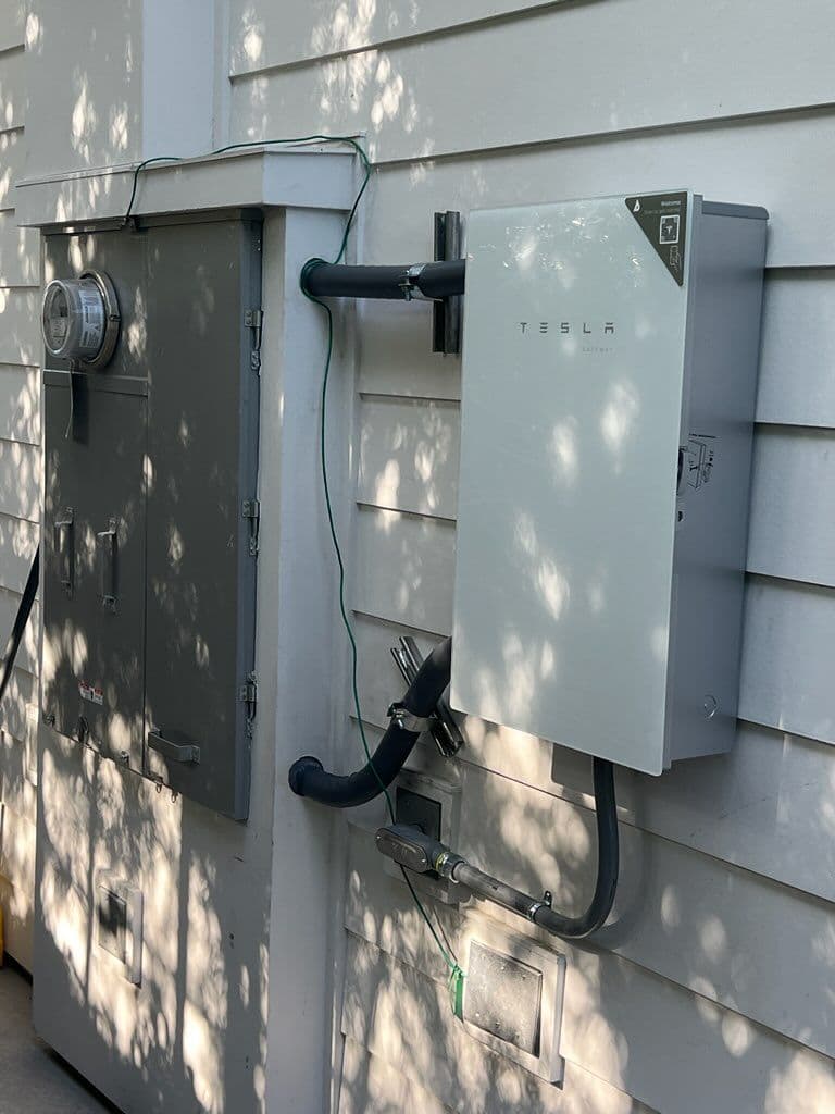 Tesla powerwall installation next to electric meter on a home exterior wall.