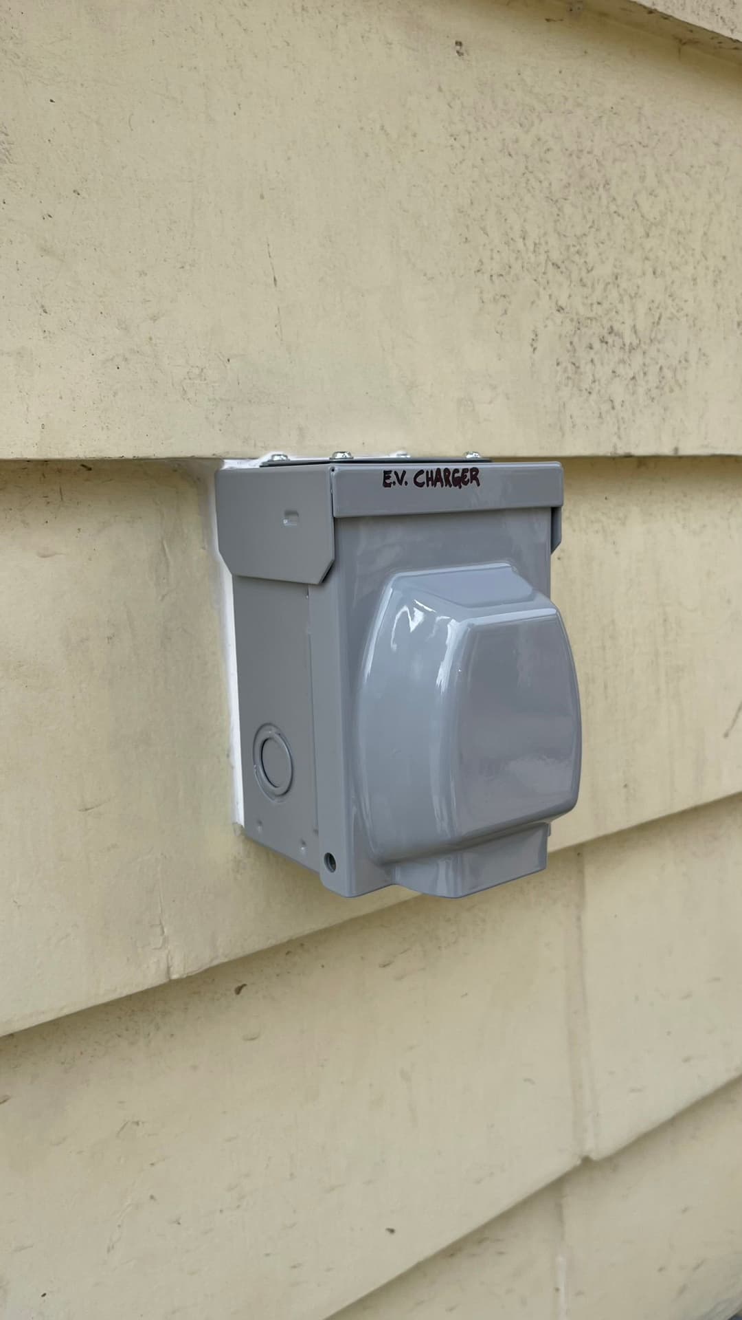 Gray EV charger mounted on a beige wall, labeled 'EV Charger'.