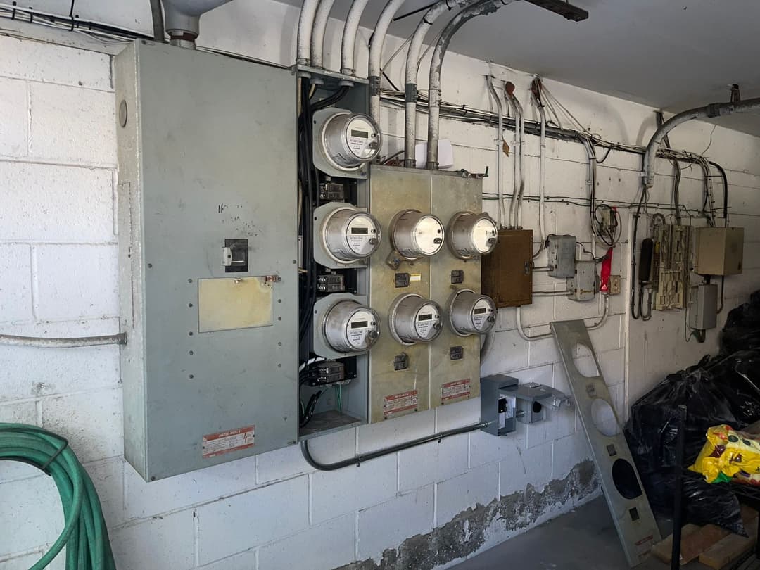 Utility meters mounted on a wall in a garage, with electrical panels and wires visible.