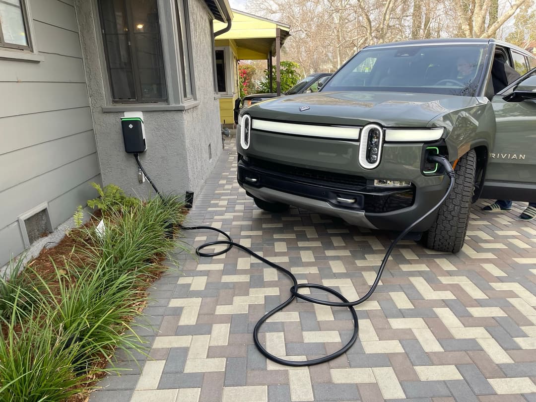 Electric vehicle charging at home with a Rivian truck plugged in beside a charging station.