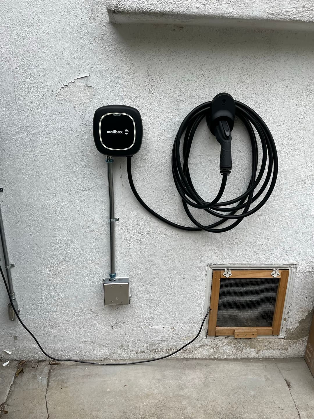 Wall-mounted electric vehicle charger with cable neatly coiled next to a vented panel.