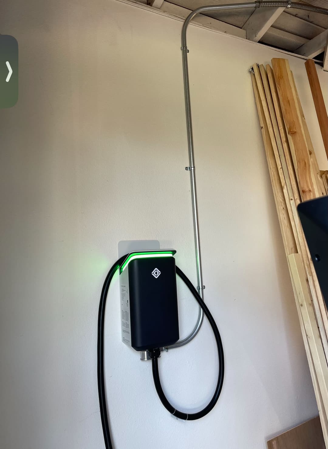 Wall-mounted electric vehicle charger with a green indicator light and connected wiring.