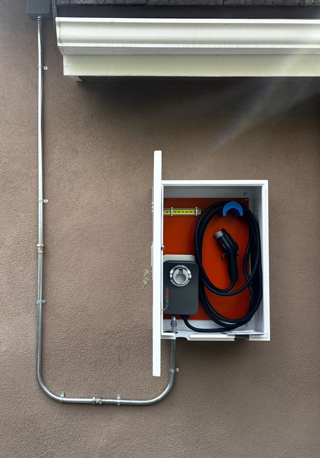 Wall-mounted electric vehicle charging station with cable and gauge.