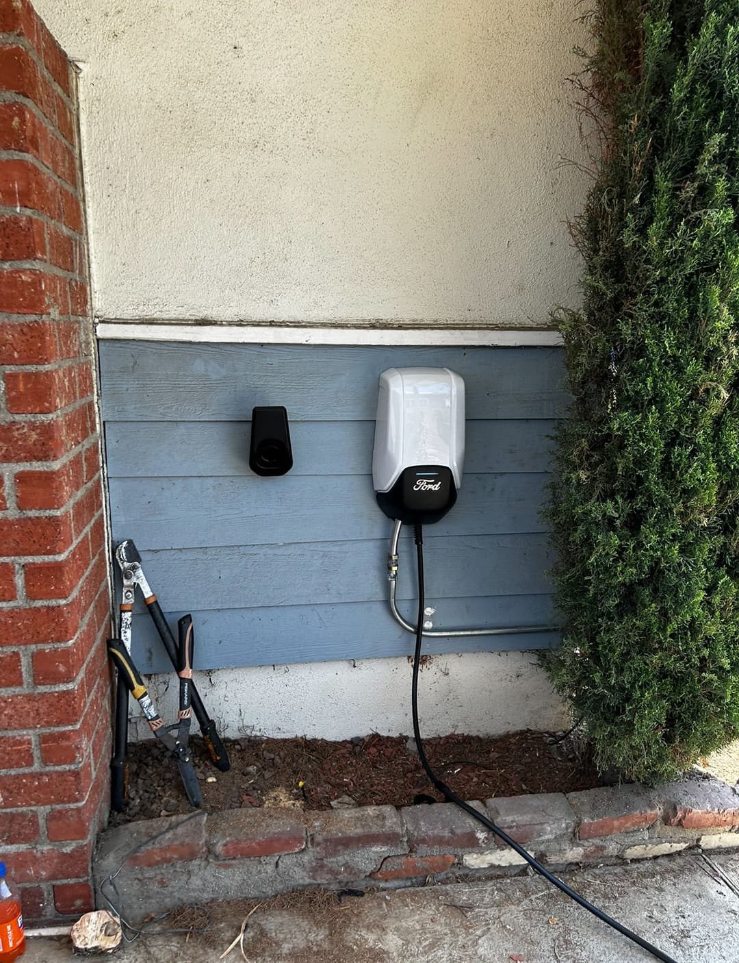 Ford electric vehicle charging station mounted on a wall next to landscaping tools.