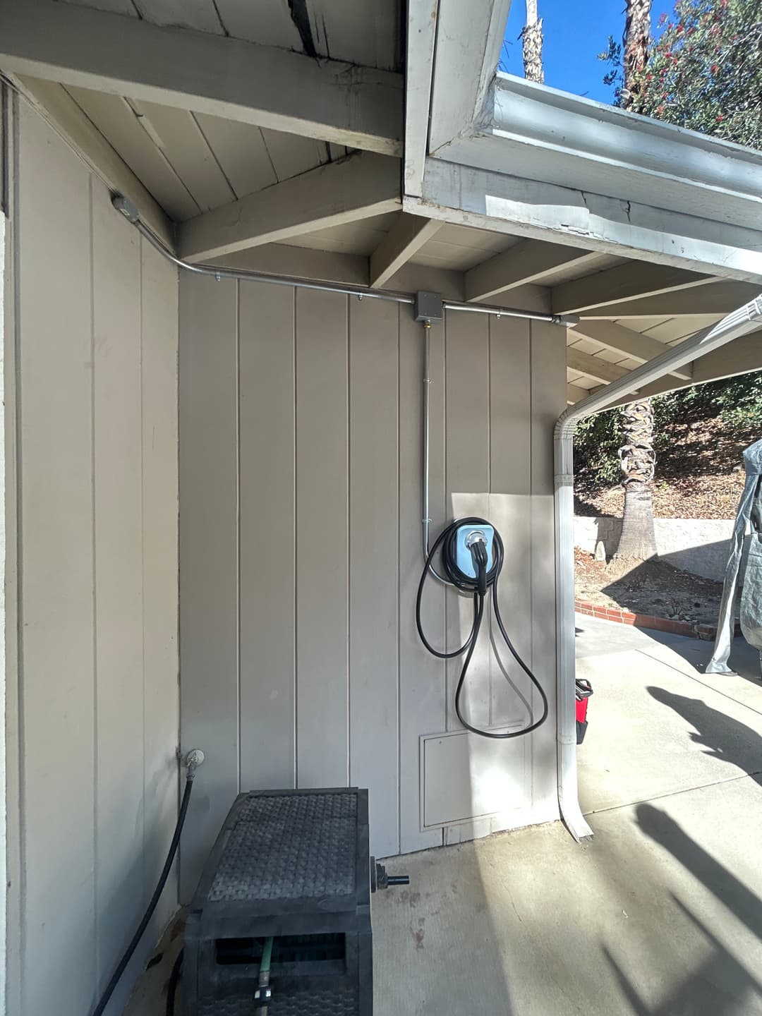 Electric vehicle charger mounted on exterior wall beside a storage box in a driveway setting.