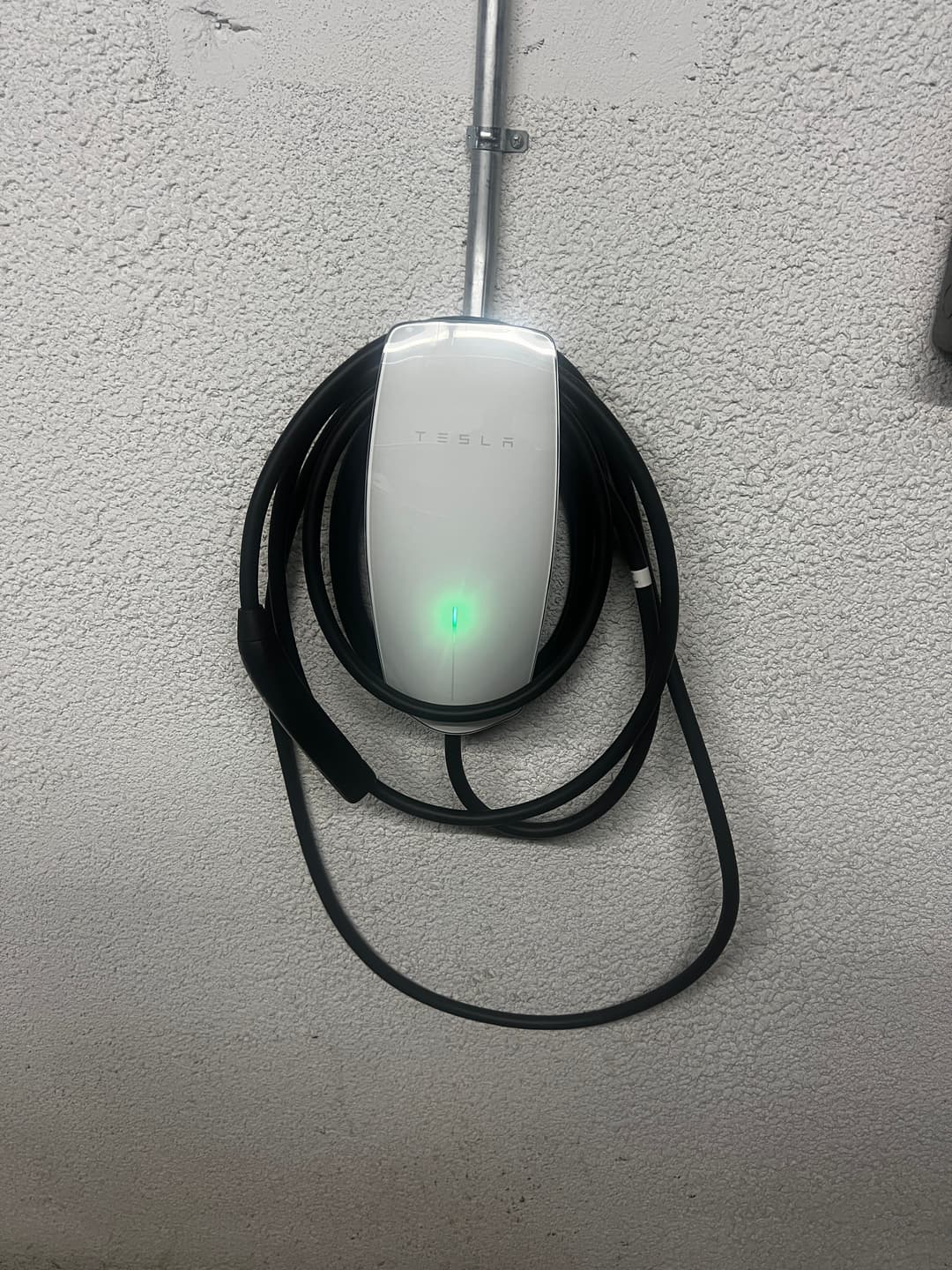 Tesla EV charger mounted on a wall with a charging cable and green indicator light.