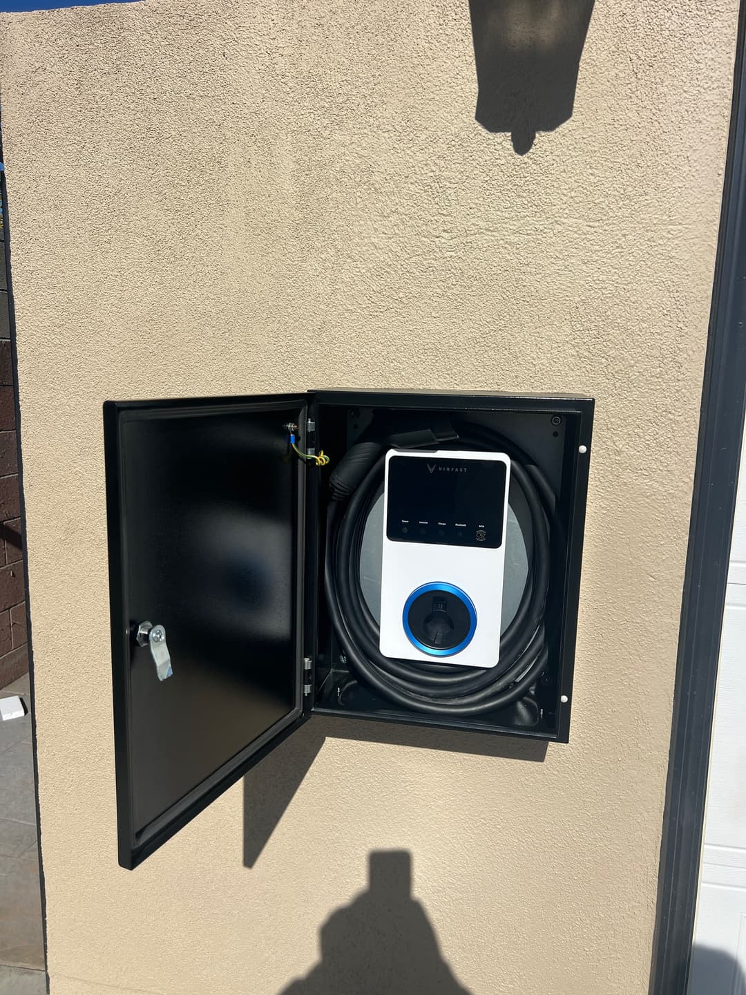 Electric vehicle charging station mounted on wall with coiled cable inside protective cabinet.