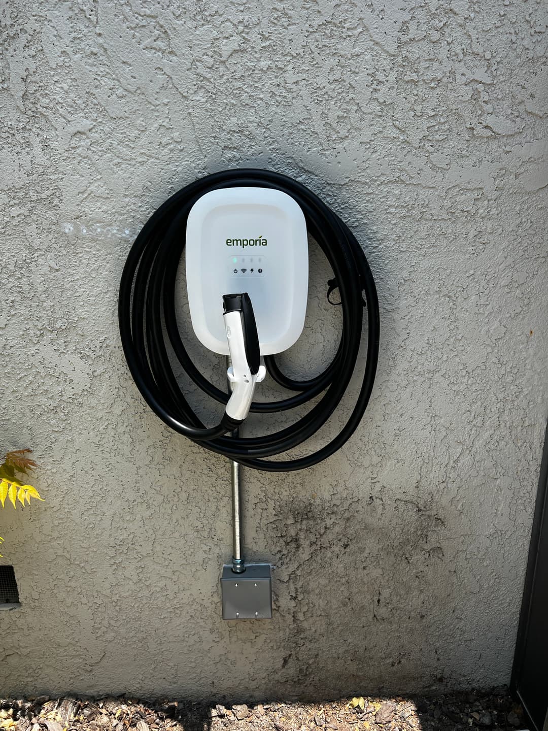 Emporia EV charger mounted on wall with coiled cable for electric vehicle charging.