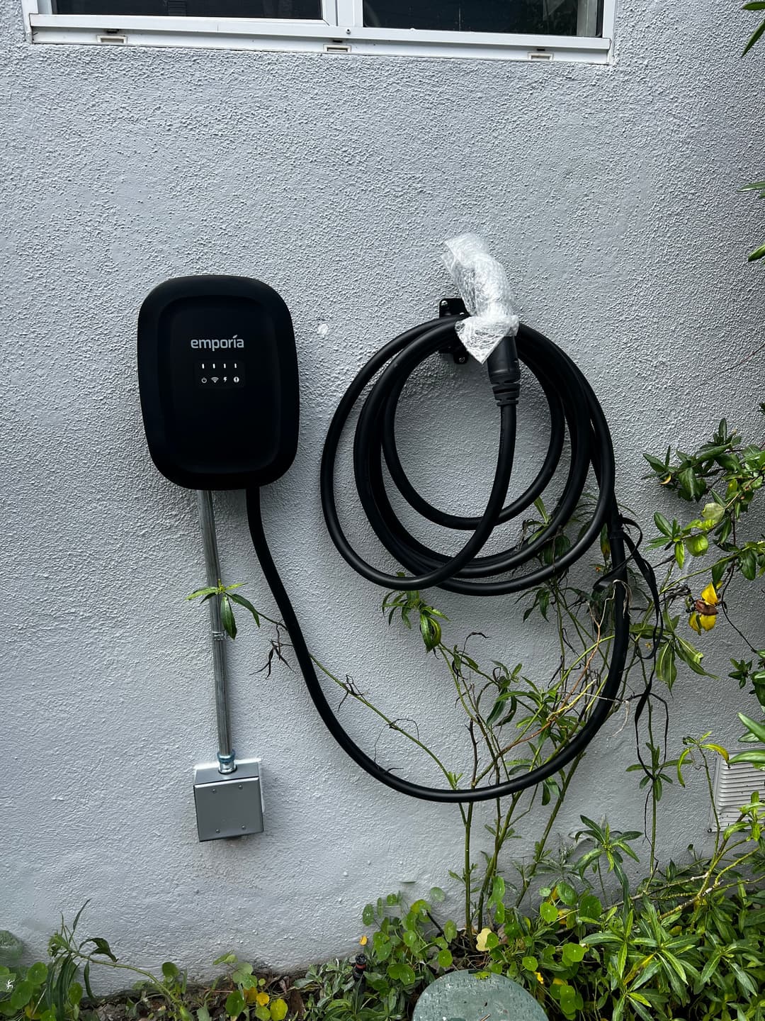 Emporia electric vehicle charger mounted on a wall with a charging cable coiled beside it.