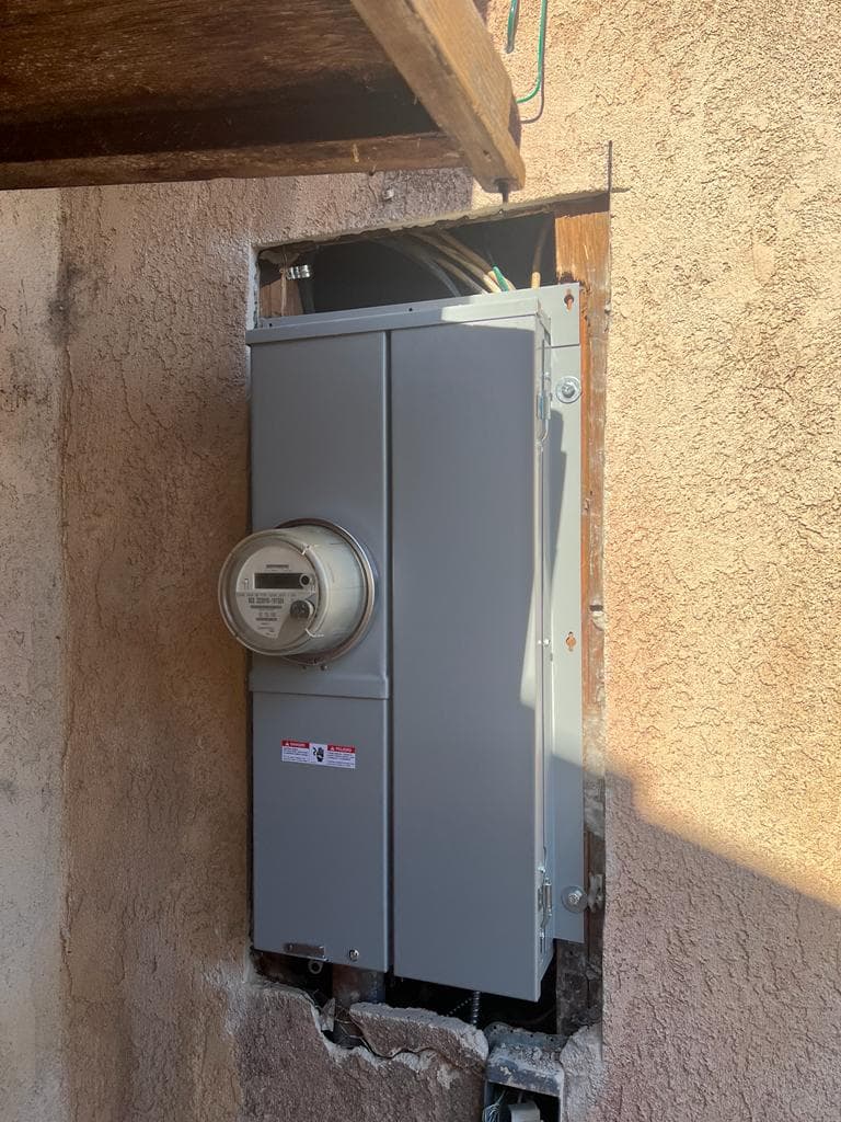 Electrical meter and service panel installed in an exterior wall with exposed wires.