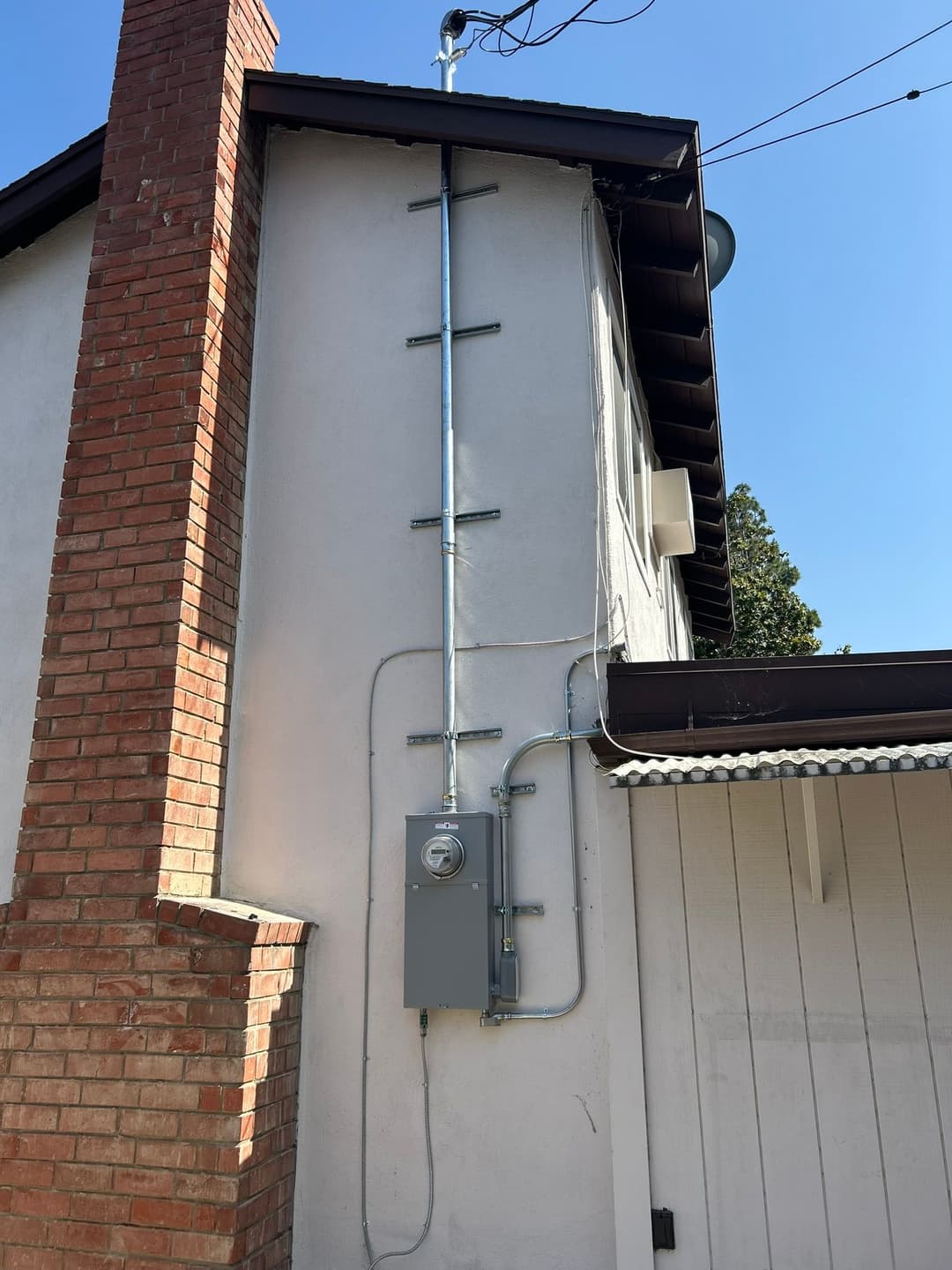 Electrical meter and conduit mounted on a wall of a residential building. Clear blue sky.