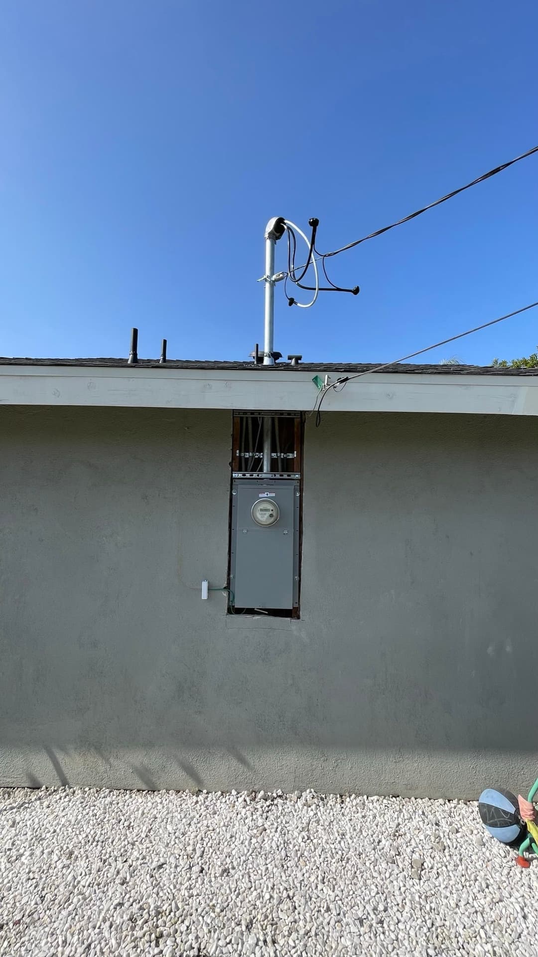 Weather station mounted on a residential wall with electrical meter and clear blue sky.