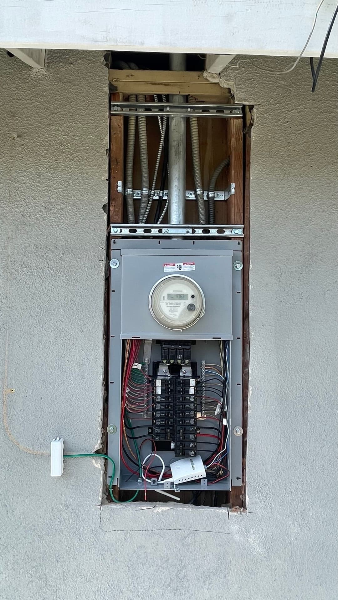 Electrical meter and circuit panel installed in a wall with exposed wiring and structure.