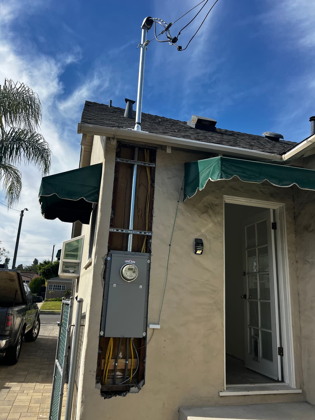 Electrical panel installation on exterior wall of a house under blue sky with power lines.