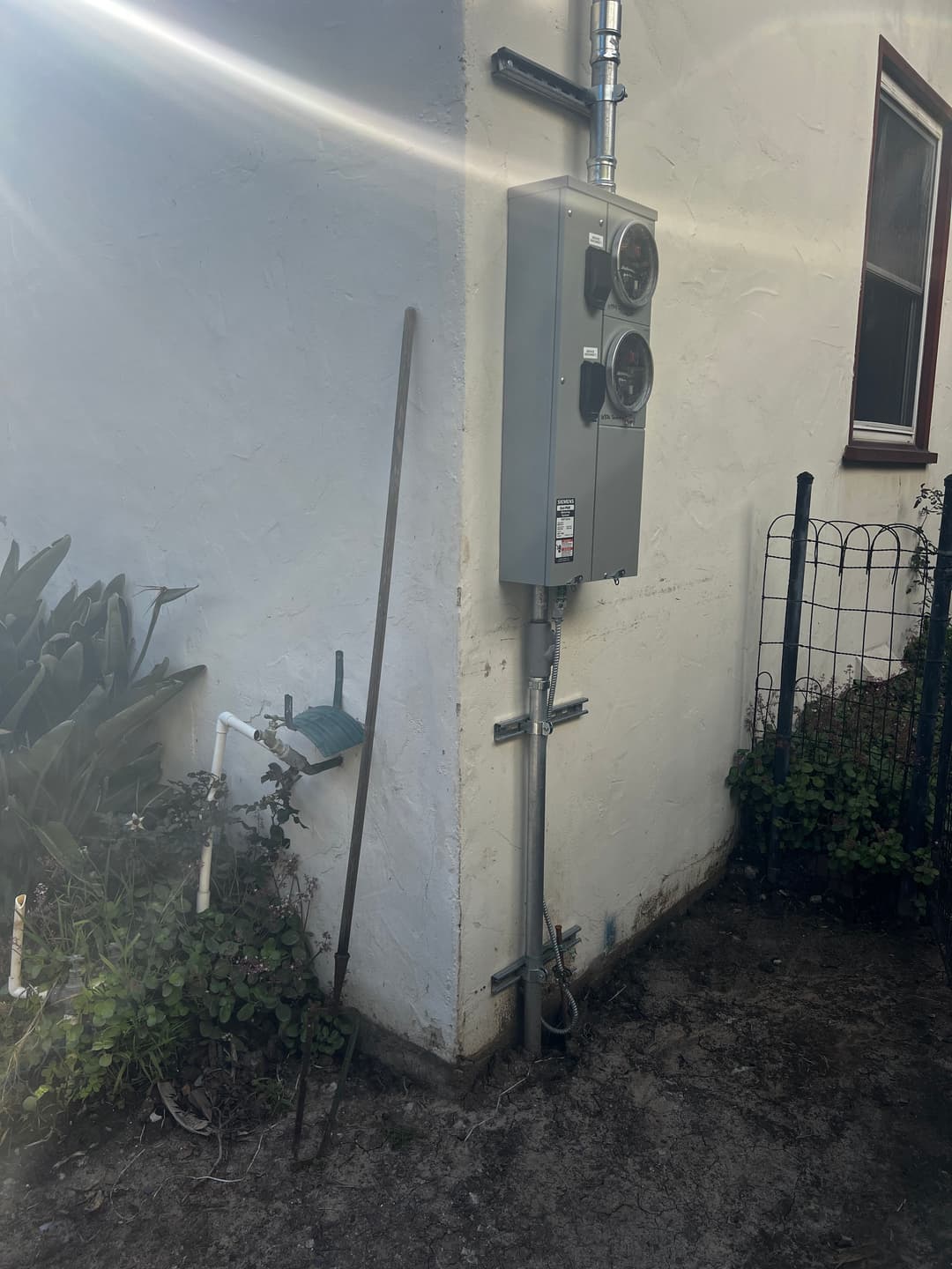 Electrical meter box mounted on a white wall with a garden stake nearby.