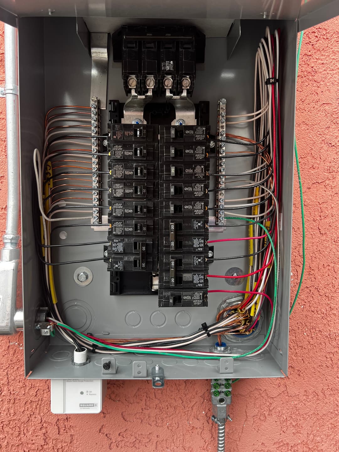 Electrical panel with breakers, wires, and connections mounted on a textured wall.