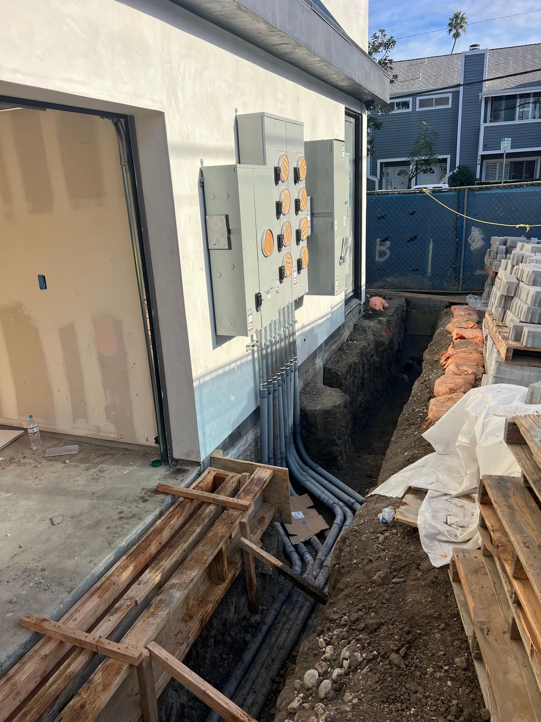 Electrical panels mounted on a wall next to a trench with PVC conduits and construction materials.