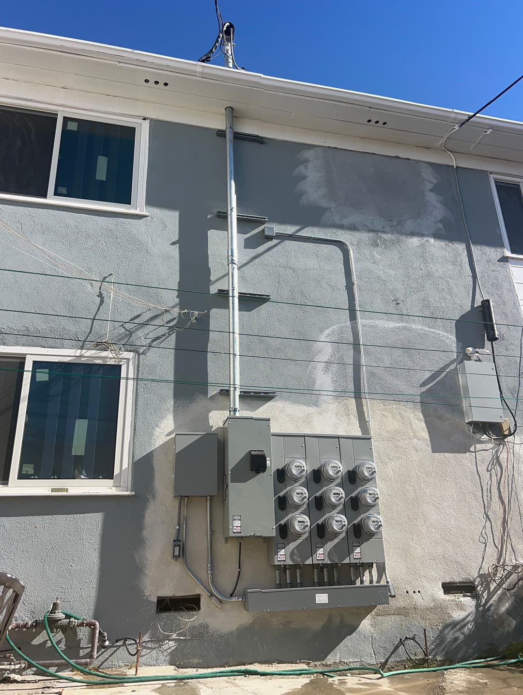 Electrical meter and service panel on the exterior wall of a house against a blue sky.