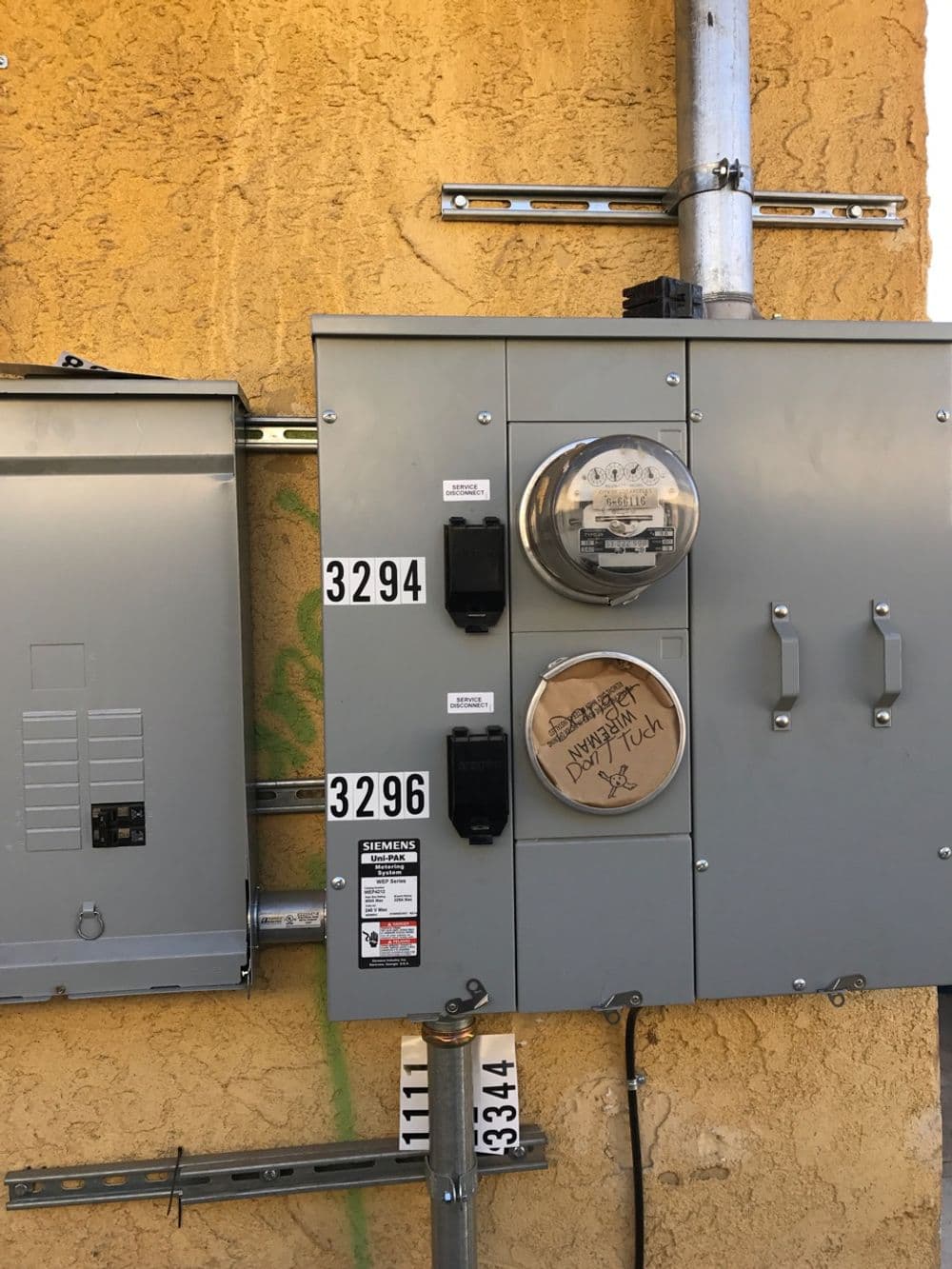 Electrical meter and service panel mounted on a textured yellow wall with labels.