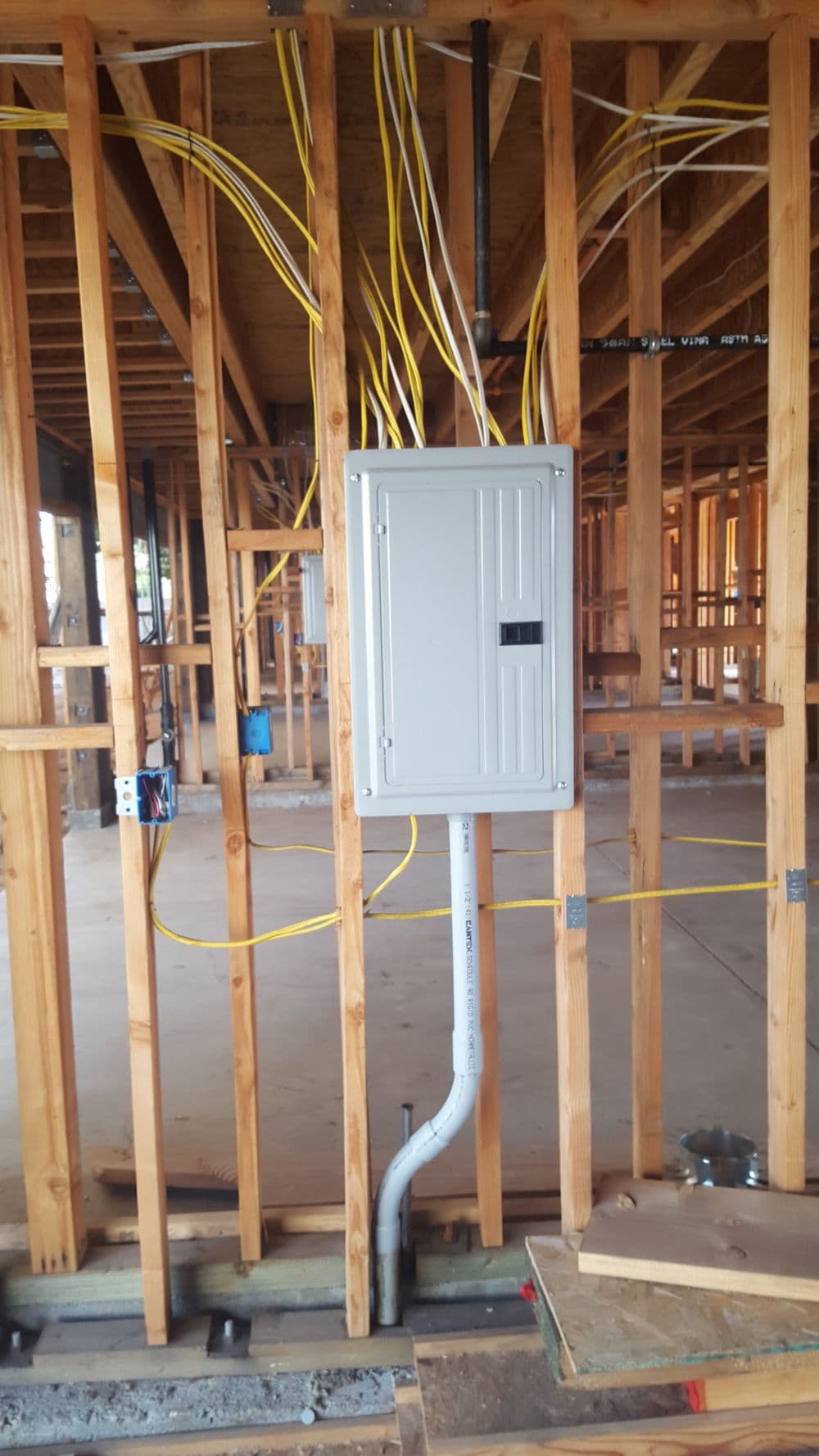Electrical panel installation with yellow wires in wooden framing of a construction site.