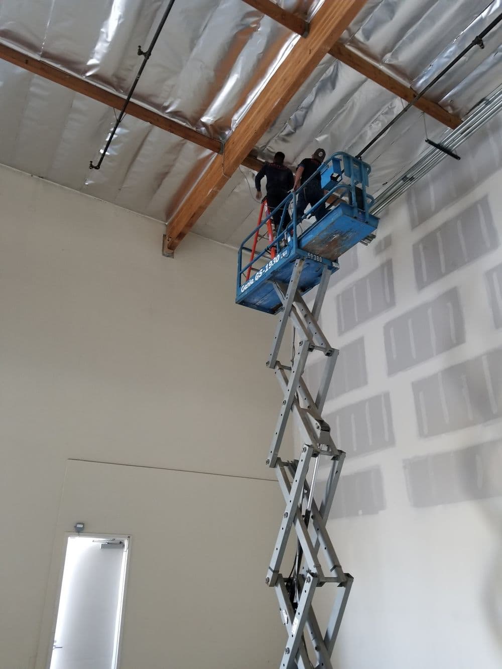 Workers on a scissor lift installing fixtures in a high-ceiling space.