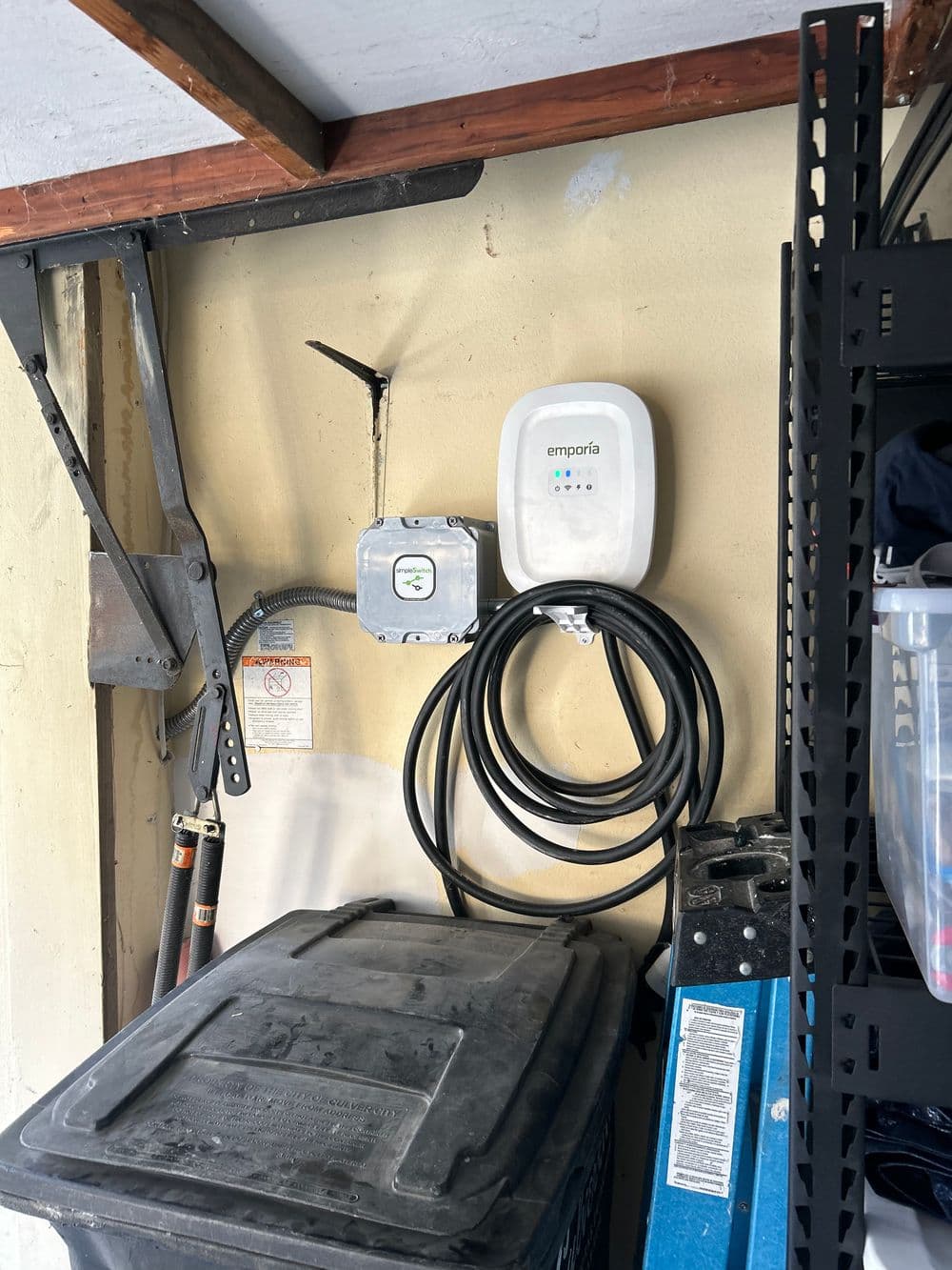 Wall-mounted EV charger with cable and electrical box in a garage setting.