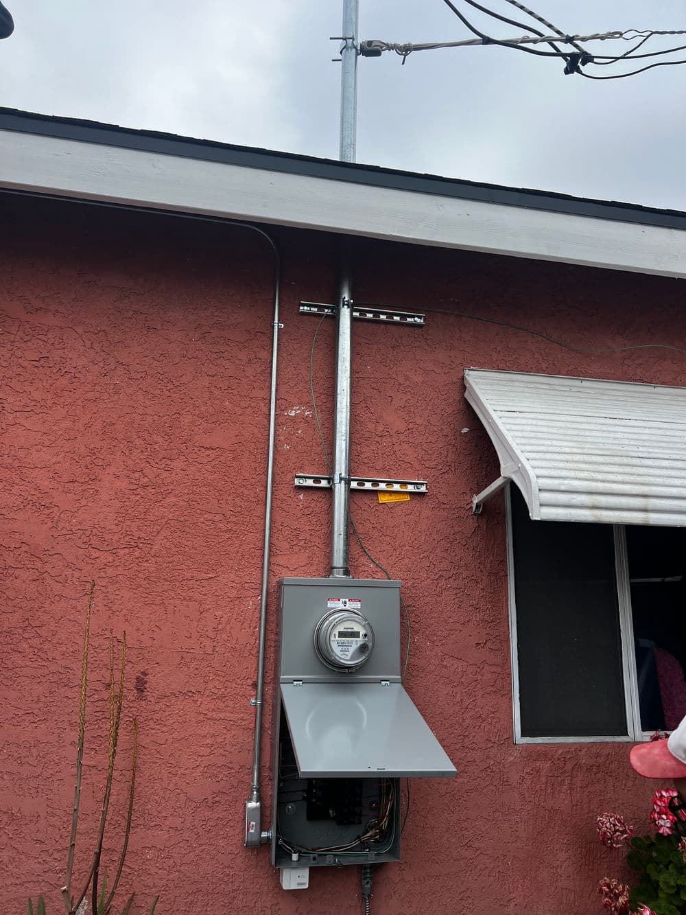 Electric meter mounted on a reddish wall with antennas and power lines above.